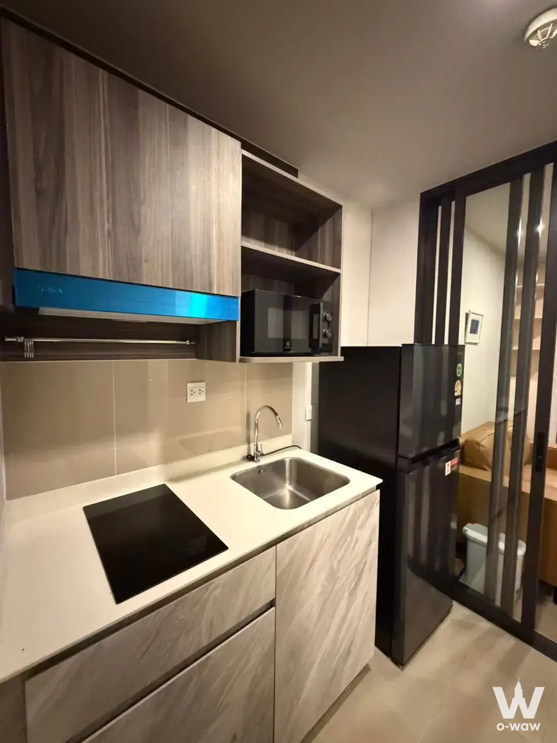Compact kitchenette in a 1-bed Aspire Onnut Station condo with a blue range hood and glass partition to a tan sofa