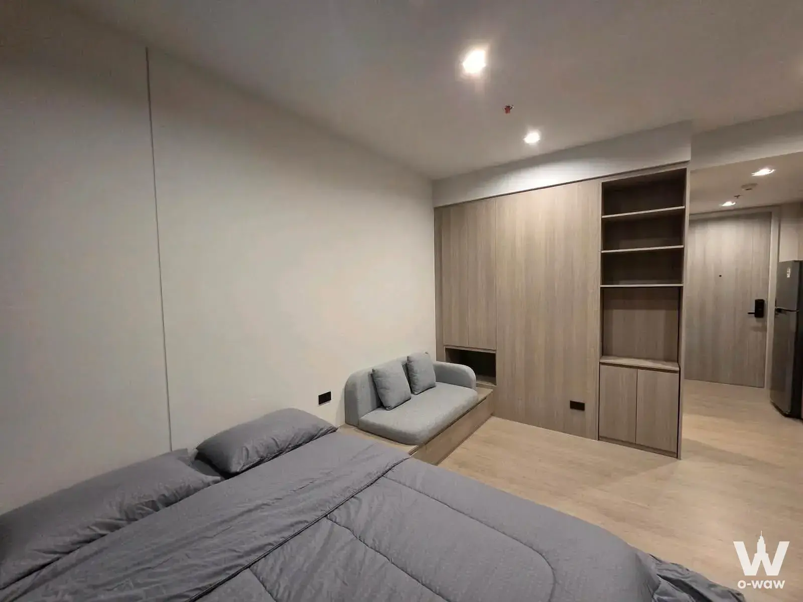 Minimalist 1-bed condo bedroom in Bangkok with grey sofa, light wood flooring, and built-in wardrobe