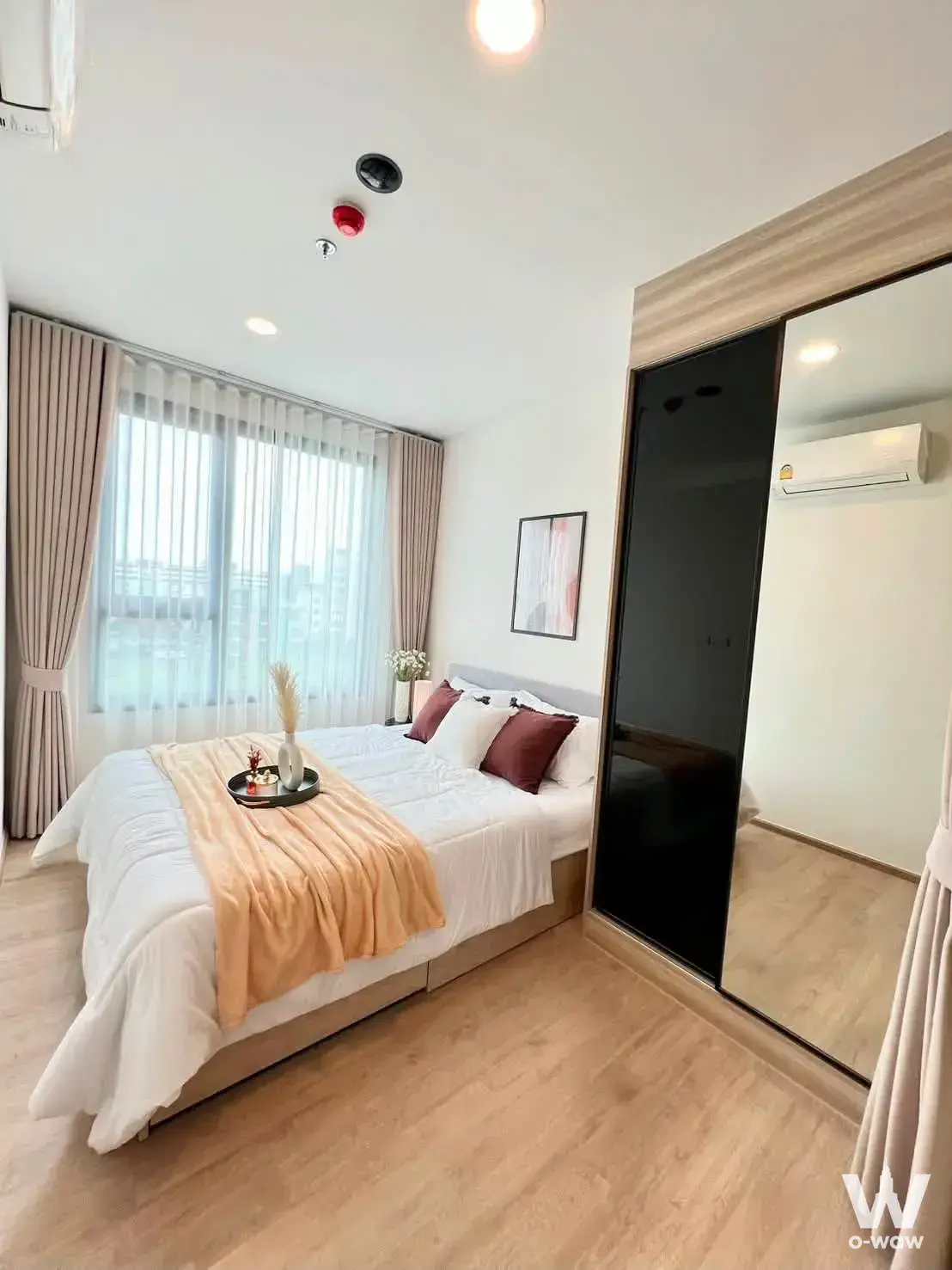 Chewathai Kaset-Nawamin 1-bed condo master bedroom with beige bedding, grey headboard, and city view