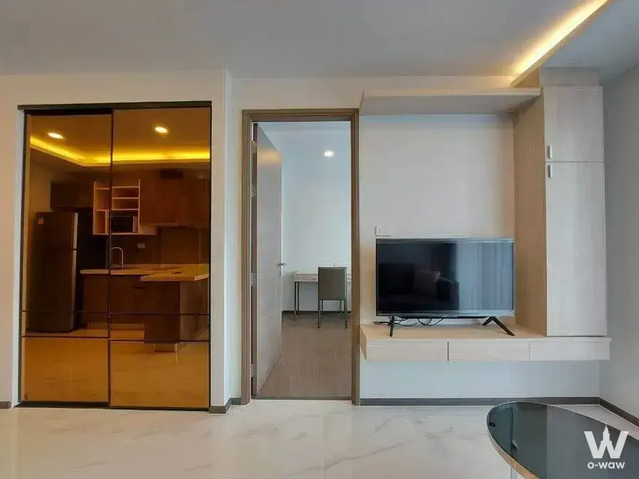 The living room in a 1-bed Define by Mayfair Sukhumvit 50 rental has a light-wood wall unit and amber glass kitchen partition