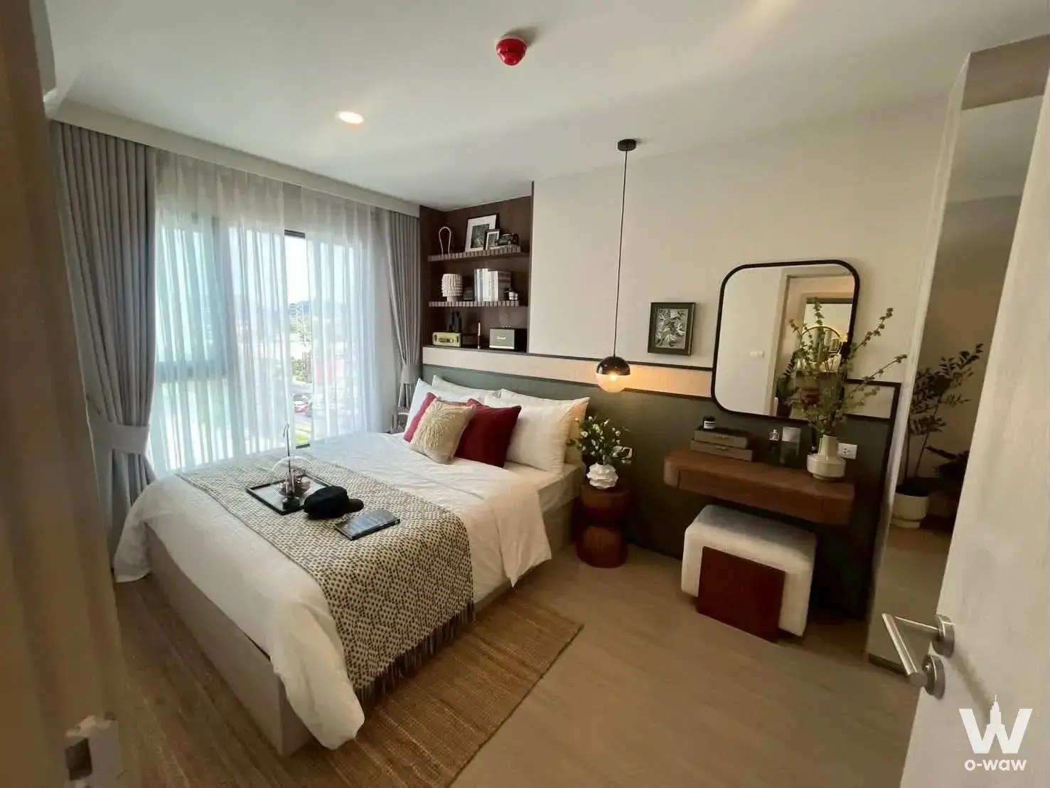 The Origin Kathu master bedroom with sage green walls, dark wood shelving, and natural light