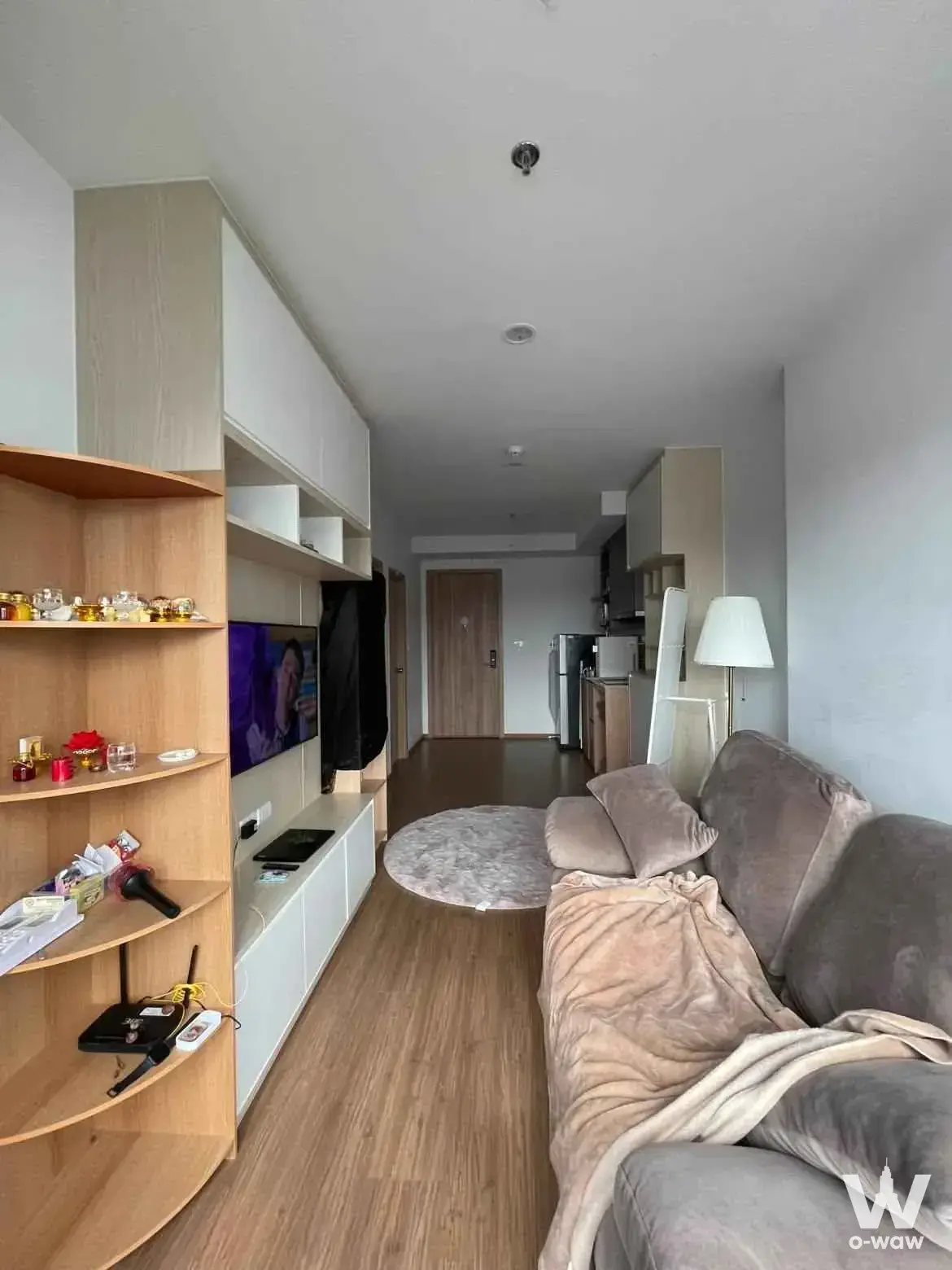 The LIVIN Phetkasem 1-bed living room with curved shelving, grey sofa, and visible kitchen area