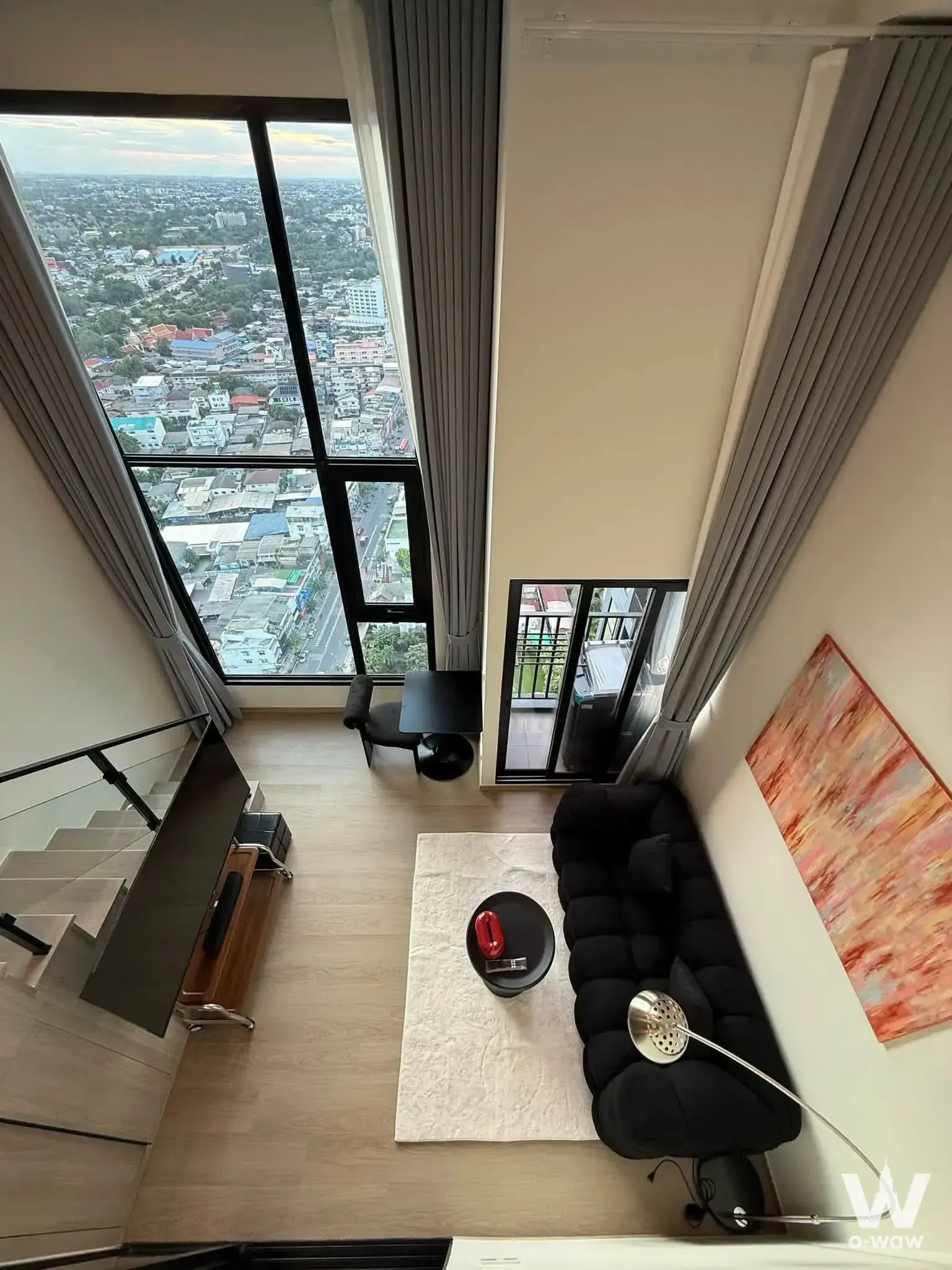 Modern living room with black sofa and city skyline view in a Bangkok Origin Play Bangkhunnon loft
