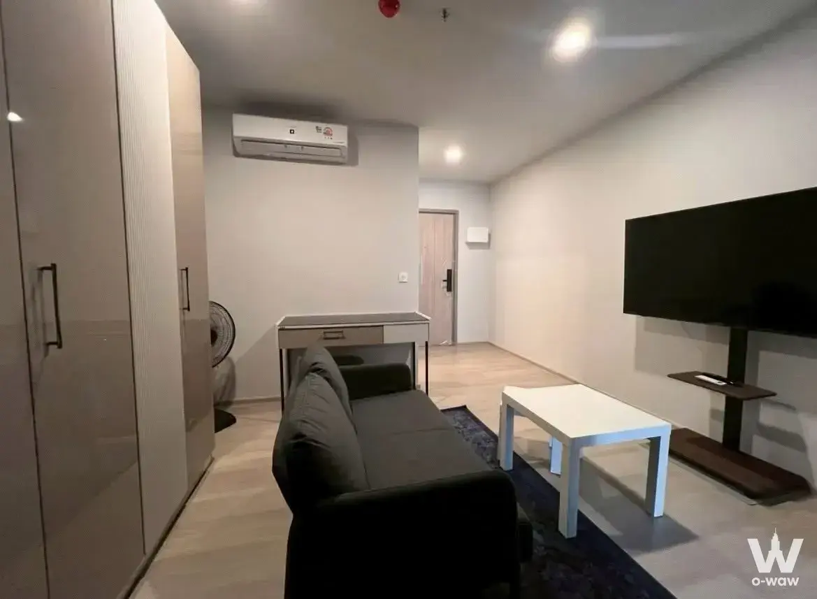 Modern 1-bed condo living room in Aspire Onnut with charcoal sofa, wall-mounted TV, and light wood flooring