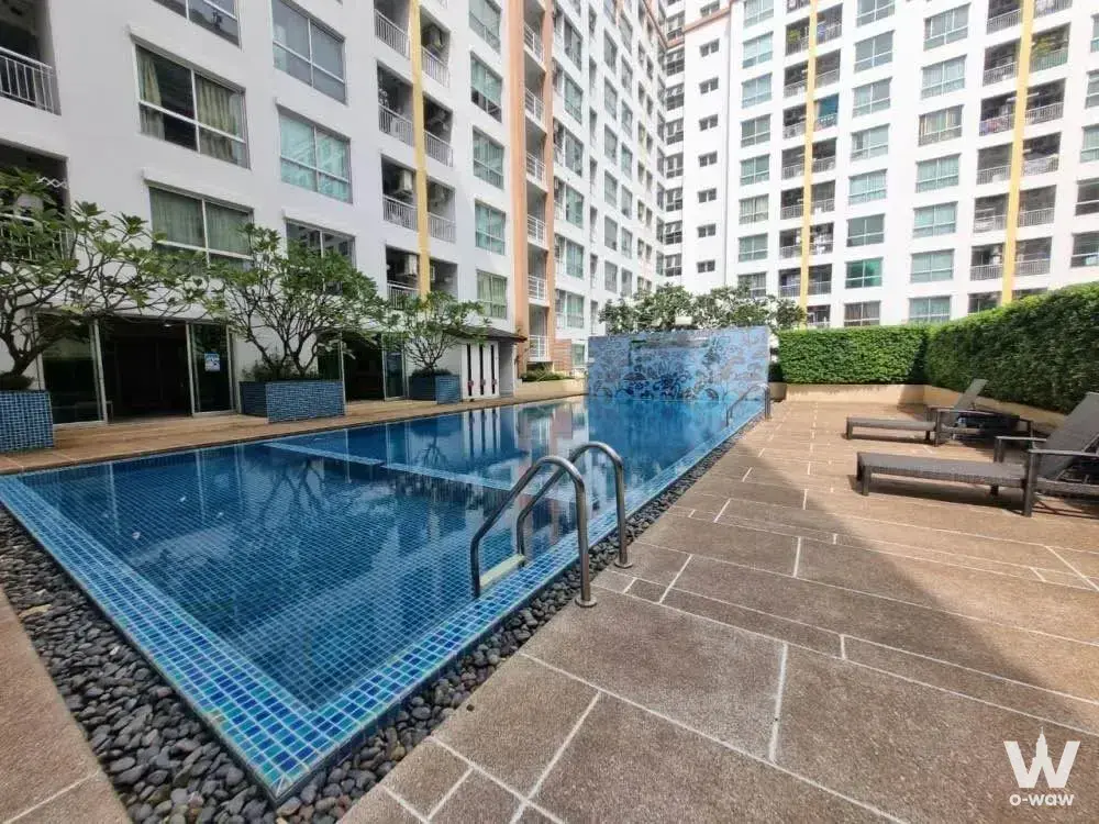 Outdoor pool at Life @Thapra 1-bed condo with blue mosaic tiles and dark wood loungers