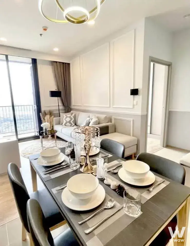 The 2-bed Oka Haus rental has an open-plan dining and living area with a dark wood table, city view and gold pendant