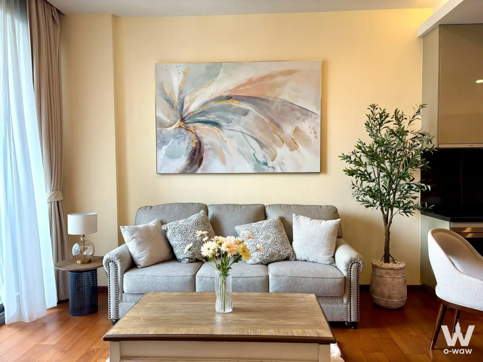 Quattro by Sansiri 1-bed condo living room featuring grey sofa, gold-framed art, and warm wood flooring
