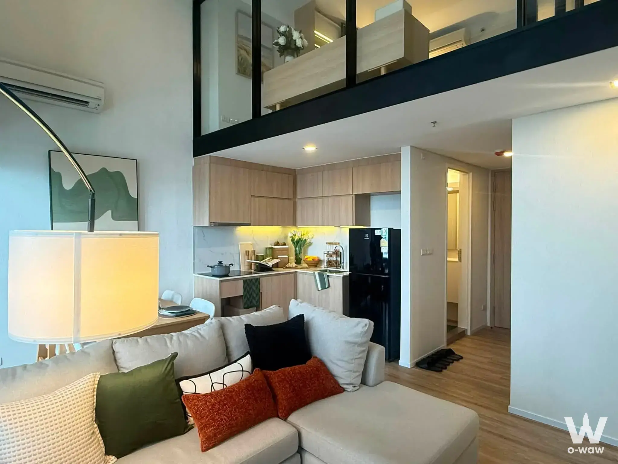 Open-plan living room in a Sukhumvit 48 condo with a sectional sofa and mezzanine loft above the kitchen