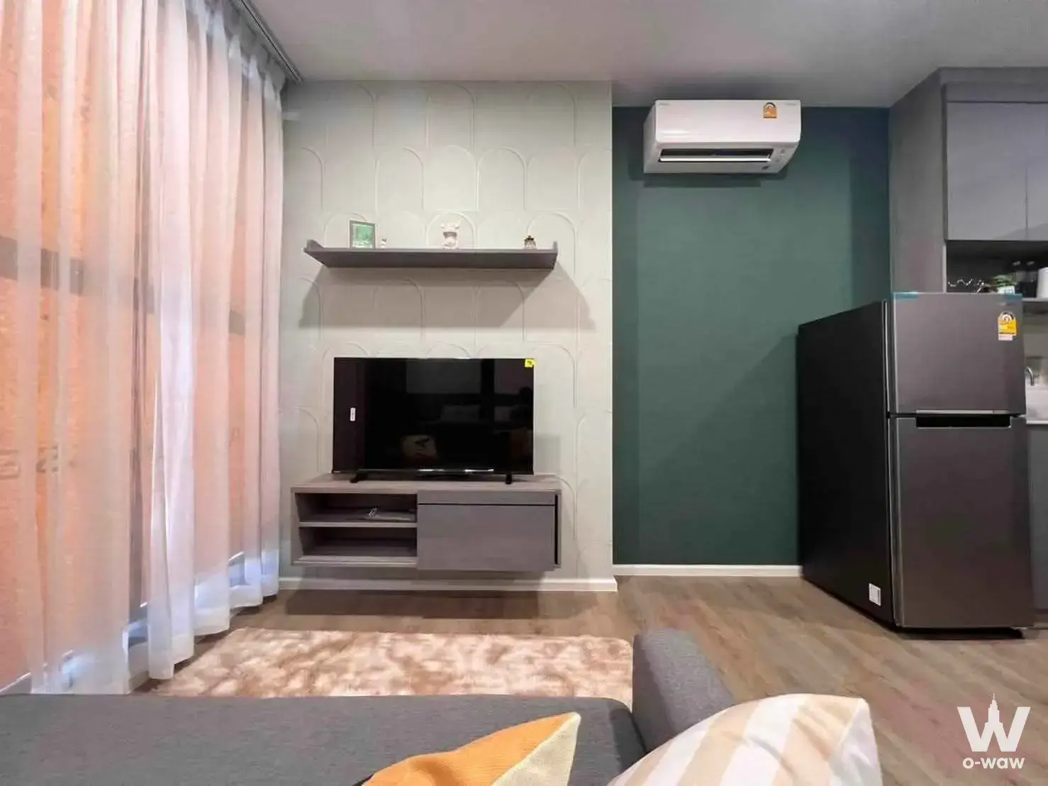 Living area in Modiz Rhythm Ramkhamhaeng 1-bed condo featuring sage green wall, grey sofa and TV console