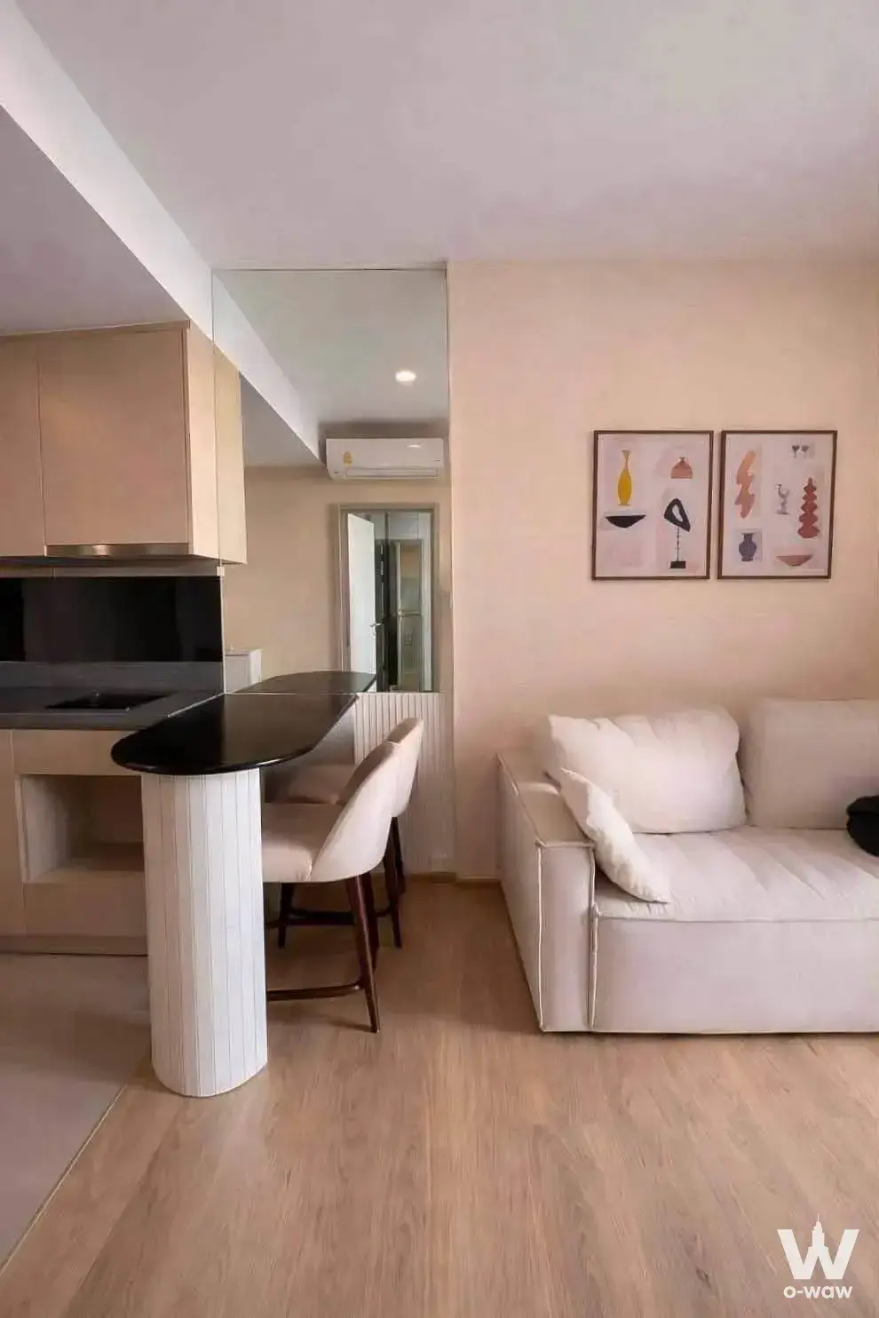 Open kitchen-living space in a 1-bed condo for sale at Oka Haus with cream cabinets and a black countertop