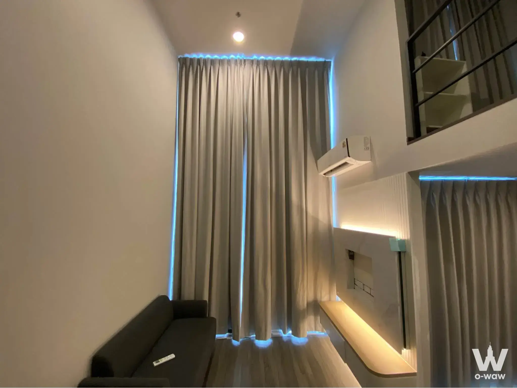 Loft-style living area in a 1-bed condo at Ideo Ramkhamhaeng Lamsali with grey sofa and blue LED strip lighting