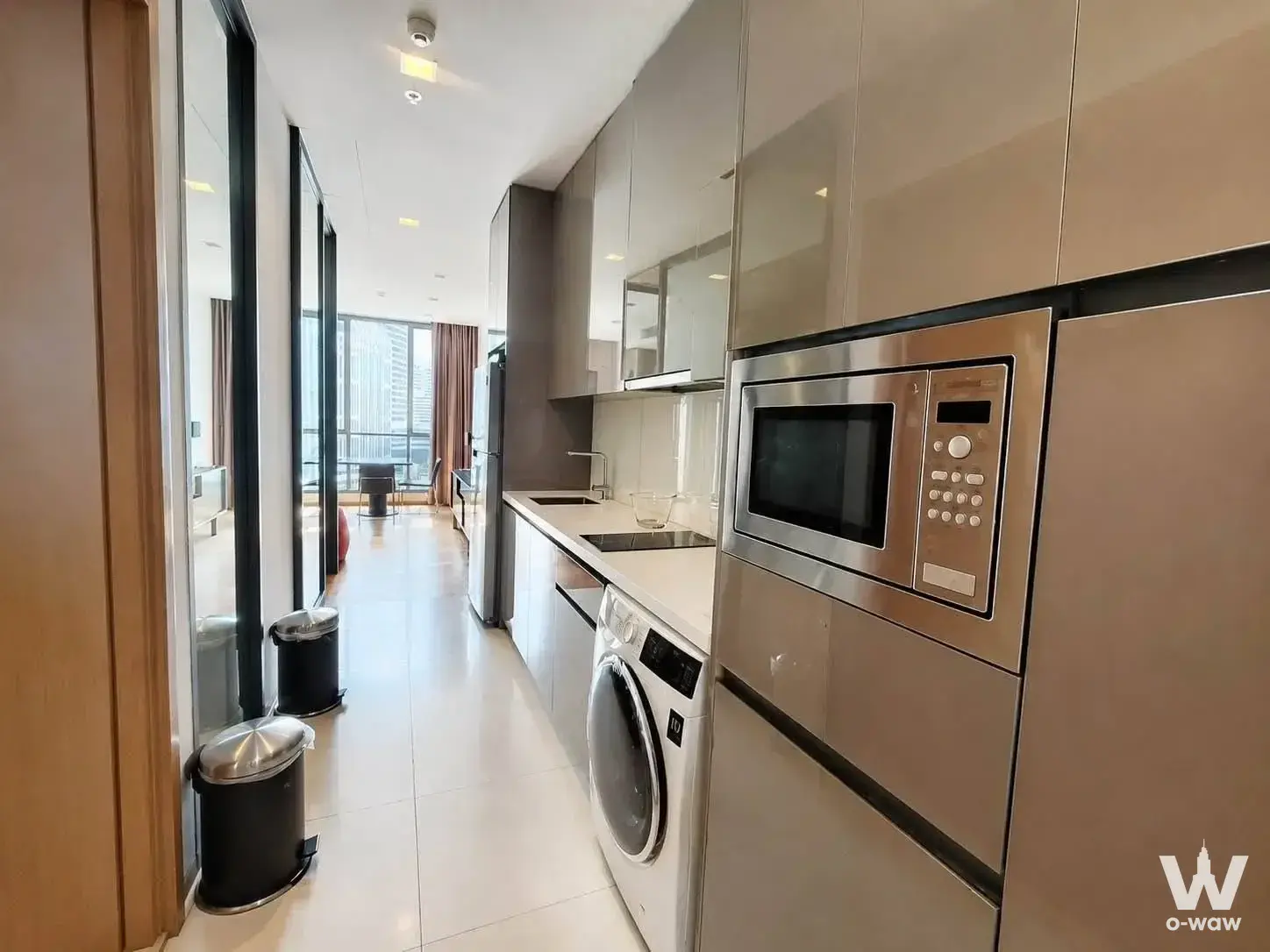 Galley kitchen in a Hyde Sukhumvit 13 rental with taupe cabinets, quartz counters, and glass doors revealing the city skyline