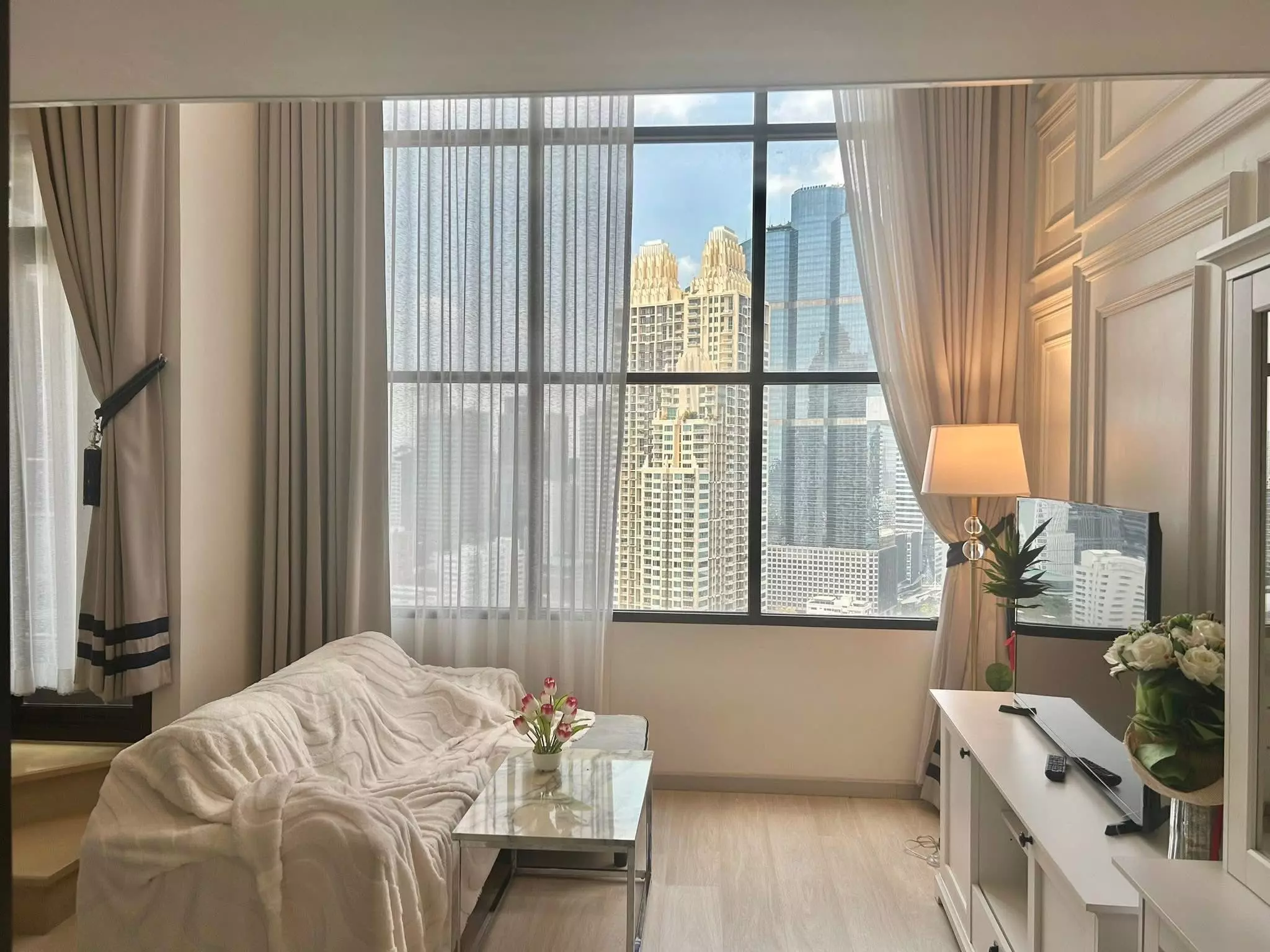 Living room with city skyline view through floor-to-ceiling windows in a 1-bed condo for rent at KnightsBridge Prime Sathon