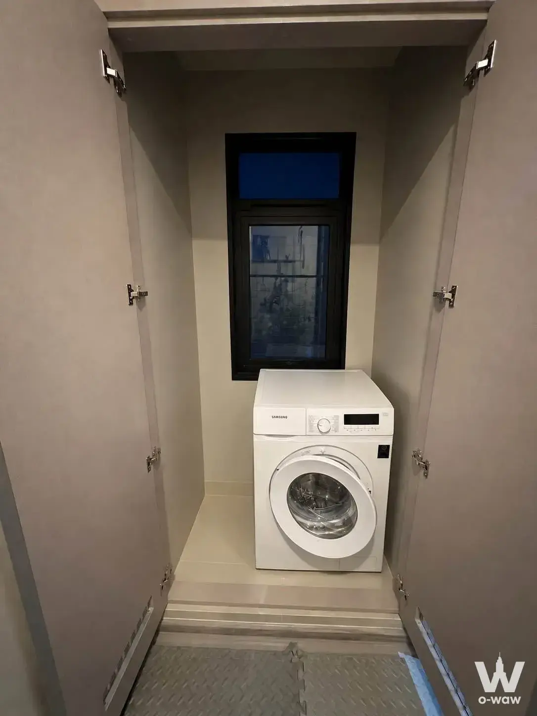 The compact laundry closet in a 2-bed Aspire Asoke-Ratchada condo for sale has a white washer and black-framed window