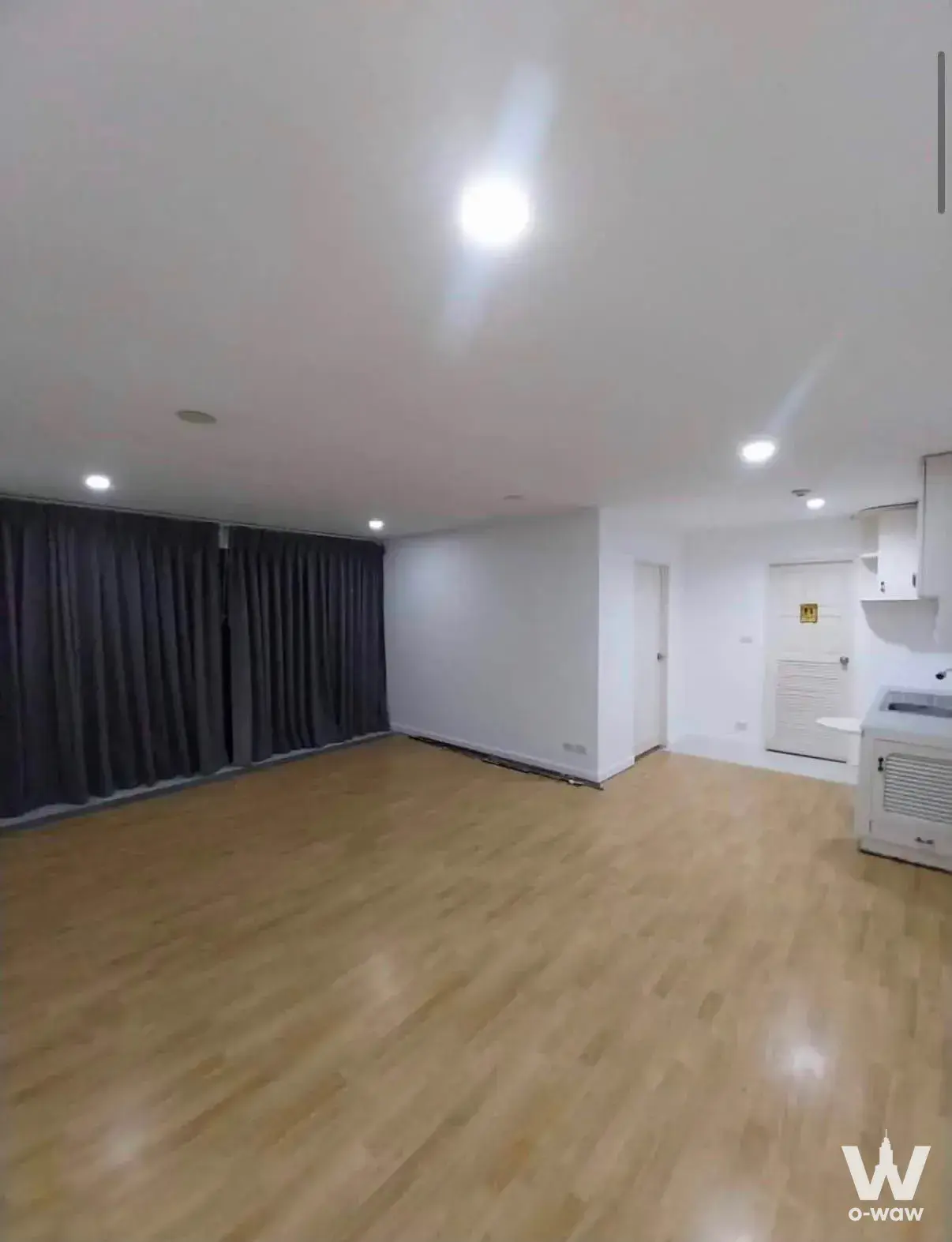 Empty 1-bed condo for sale in Ratchada Pavillion Condo with light wood flooring and charcoal grey curtains