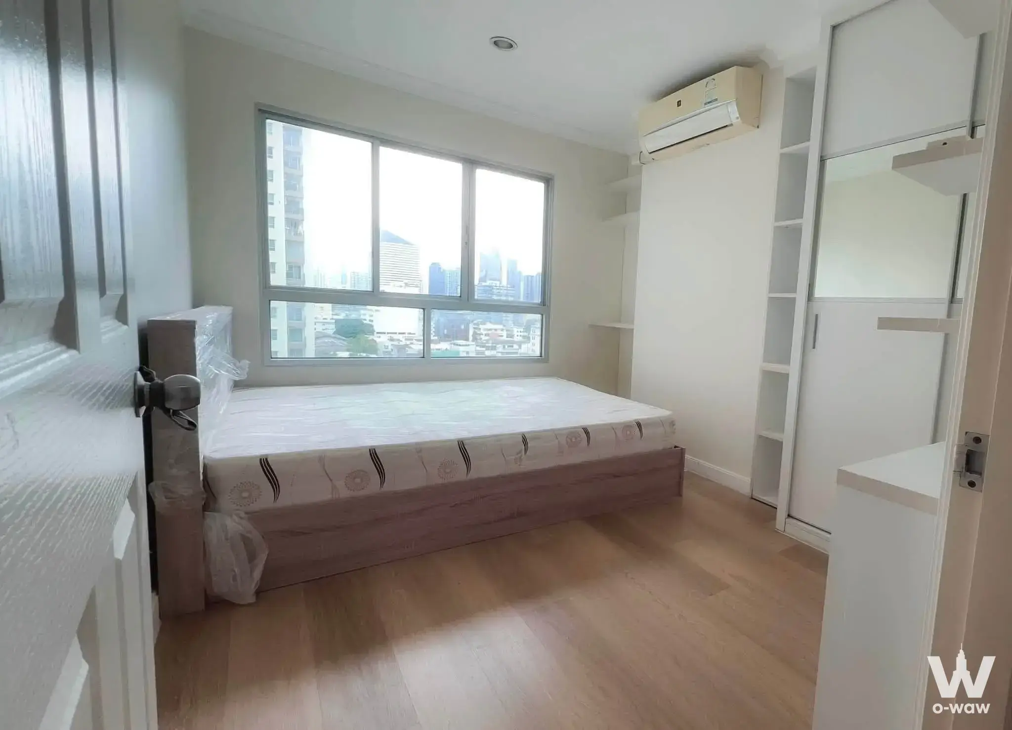 Unfurnished bedroom in Lumpini Place Rama 8 with a wooden queen bed, built-in shelving, and a large sliding window